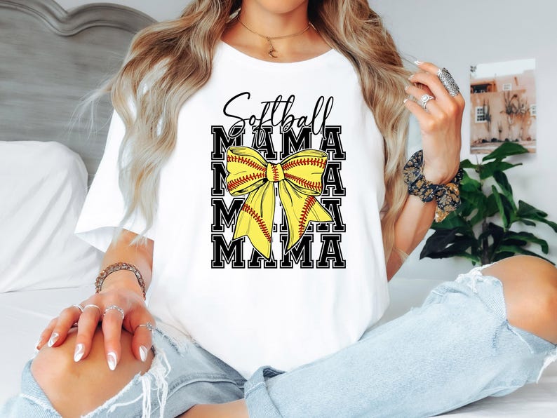 K&ouml;nnte beinhalten: Wei&szlig;es T-Shirt mit dem Text "Softball Mama" in schwarzen Buchstaben und einer gelben und roten Softball-Schleife.