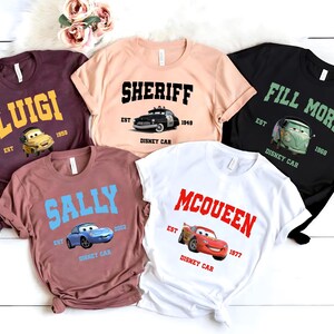 May include: Five different t-shirts featuring characters from the Disney Pixar movie Cars. The shirts are maroon, peach, black, brown, and white. Each shirt has a different character and the text "Disney Car" printed on it.