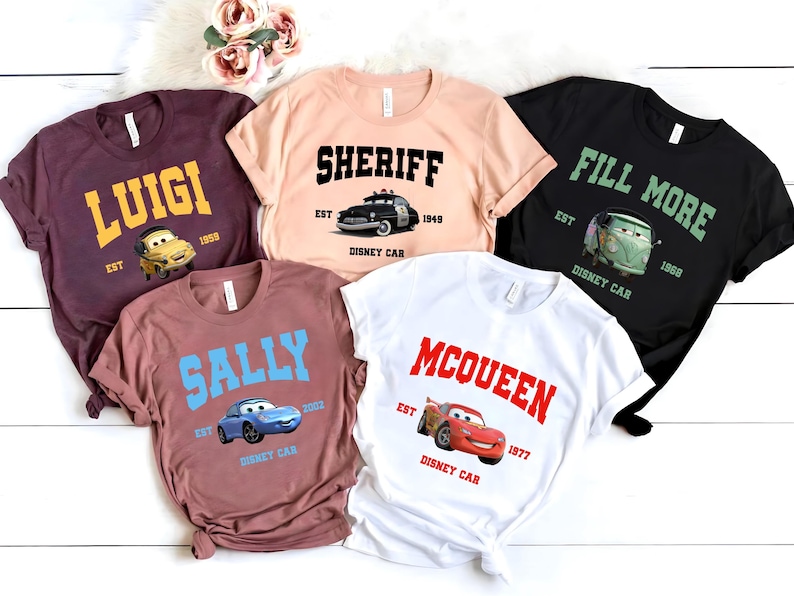 May include: Five different t-shirts featuring characters from the Disney Pixar movie Cars. The shirts are maroon, peach, black, brown, and white. Each shirt has a different character and the text "Disney Car" printed on it.