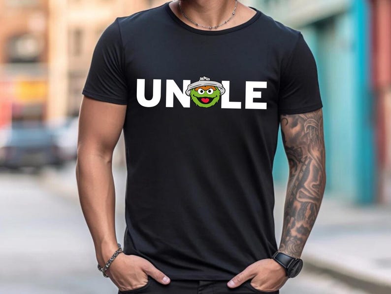 May include: Black t-shirt with the word "UNCLE" in white block letters. The "O" in "UNCLE" is replaced with a cartoon character's face. The character is green with a white hat.