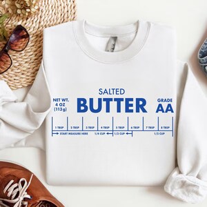 May include: White sweatshirt with the words "SALTED BUTTER" in blue, along with a measurement guide. The sweatshirt also has the text "NET WT. 4 OZ (113g)" and "GRADE AA".