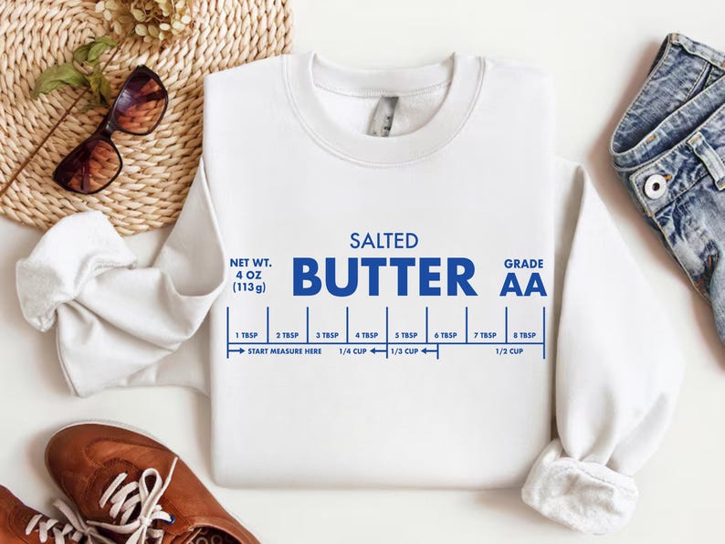 May include: White sweatshirt with the words "SALTED BUTTER" in blue, along with a measurement guide. The sweatshirt also has the text "NET WT. 4 OZ (113g)" and "GRADE AA".