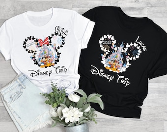 May include: Two black and white t-shirts with a Mickey Mouse ear design featuring a castle, fireworks, and the text "Disney Trip" and the year "2025". One shirt has the name "Olivia" and the other has the name "Lucas".