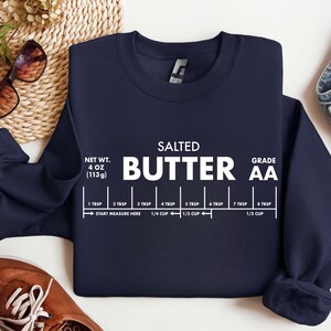 May include: Navy blue sweatshirt with the words "SALTED BUTTER" in white, along with a butter measurement guide. The sweatshirt also displays the net weight of 4 oz (113g) and the grade AA.