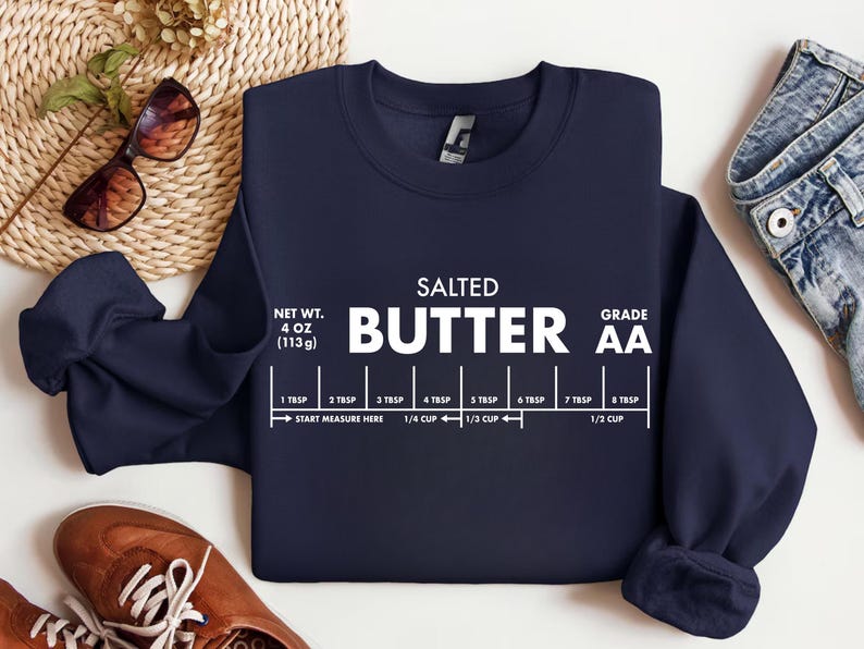 May include: Navy blue sweatshirt with the words "SALTED BUTTER" in white, along with a butter measurement guide. The sweatshirt also displays the net weight of 4 oz (113g) and the grade AA.