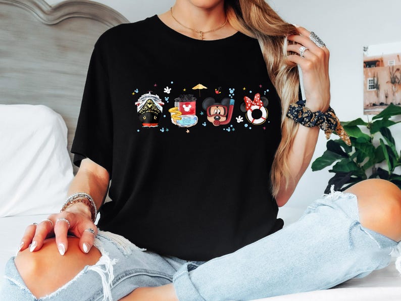 May include: Black t-shirt featuring a colourful graphic of Mickey Mouse and his friends on a boat, a beach umbrella, and a life preserver. The graphic includes the text "Mickey Mouse" and "Disney".