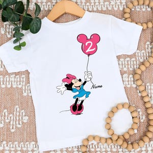 May include: White t-shirt with a pink Minnie Mouse holding a pink balloon with the number 2 on it. The text "Name" is printed on the shirt.