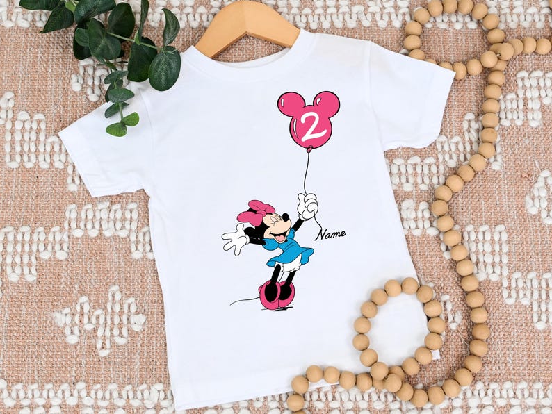 May include: White t-shirt with a pink Minnie Mouse holding a pink balloon with the number 2 on it. The text "Name" is printed on the shirt.