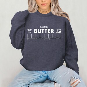 May include: A navy blue sweatshirt with the words "SALTED BUTTER AA" printed in white. Below the text is a butter measurement guide, with measurements from 1 tablespoon to 1/2 cup. The net weight is 4 oz (113g).
