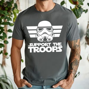 May include: A dark grey t-shirt with a white graphic of a Star Wars Stormtrooper helmet with the text "SUPPORT THE TROOPS" underneath.