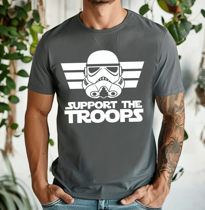 May include: A dark grey t-shirt with a white graphic of a Star Wars Stormtrooper helmet with the text "SUPPORT THE TROOPS" underneath.