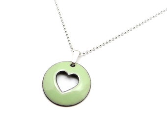 May include: A silver chain necklace with a light green pendant. The pendant is a circle with a heart cut out of the centre.