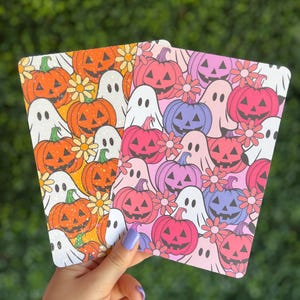 May include: Two Halloween-themed decorative cards. One card features orange pumpkins, white ghosts, and yellow flowers on a yellow background. The other card has pink, purple, and red pumpkins, white ghosts, and pink flowers on a pink background.