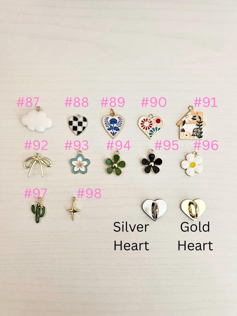 May include: A collection of decorative charms in various shapes and colors, including a cloud, hearts, flowers, a house, a bow, a cactus, and a cross. The charms are labeled with numbers and the words "Silver Heart" and "Gold Heart".