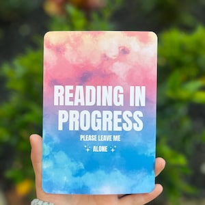 May include: A pink and blue watercolor card with the text "Reading in Progress" and "Please Leave Me Alone" with stars on either side of the word "Alone".