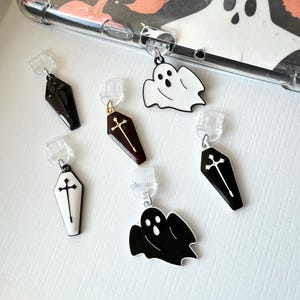 Könnte beinhalten: Sechs Halloween-Anhänger, darunter Geister und Särge, mit Kreuzdesign. Die Anhänger sind schwarz, weiß und burgunderrot mit goldenen Akzenten.