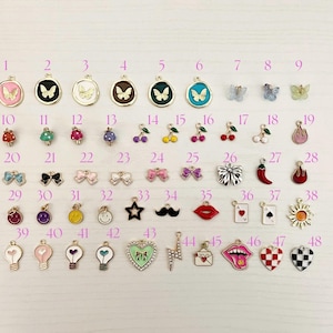May include: A collection of 48 colorful enamel charms in various shapes, including butterflies, mushrooms, cherries, bows, stars, mustaches, lips, playing cards, hearts, and lightbulbs. Each charm has a gold-tone metal border.