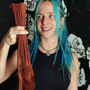 Könnte beinhalten: Eine Person mit blauen Haaren hält ein Bündel brauner synthetischer Dreadlocks. Die Dreadlocks sind etwa 50 cm lang.