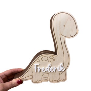 May include: Wooden dinosaur shaped piggy bank with a white name tag that says "Frederik".
