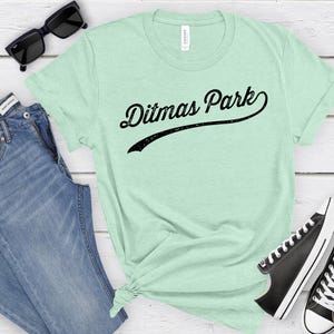 May include: A light green t-shirt with the text "Ditmas Park" in a black, curved, vintage-style font.
