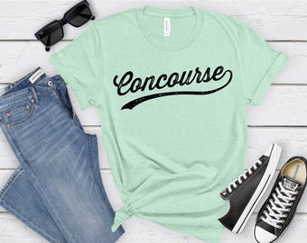 May include: A light green t-shirt with the word "Concourse" printed in black in a vintage baseball font.