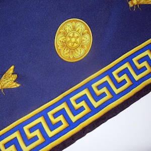 Puede incluir: Un pa&ntilde;uelo de seda azul con un borde dorado de clave griega y dise&ntilde;os florales dorados. El pa&ntilde;uelo tambi&eacute;n presenta un dise&ntilde;o de abeja.