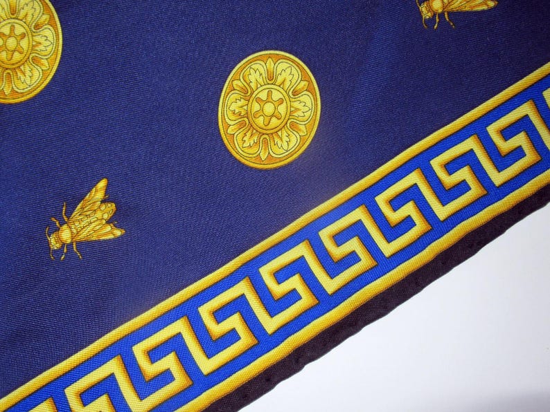 Puede incluir: Un pa&ntilde;uelo de seda azul con un borde dorado de clave griega y dise&ntilde;os florales dorados. El pa&ntilde;uelo tambi&eacute;n presenta un dise&ntilde;o de abeja.