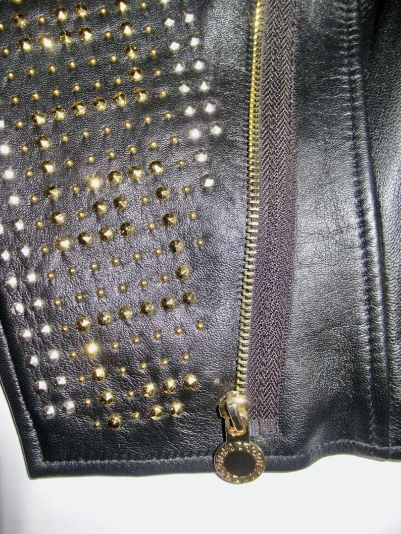 May include: Close-up of a black leather jacket with gold and silver studs. The jacket has a zipper closure with a gold zipper pull.