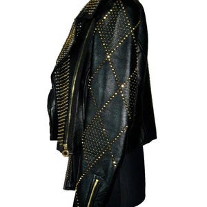 May include: A black leather jacket with a diamond pattern and gold studs. The jacket has a zip closure and a collar.