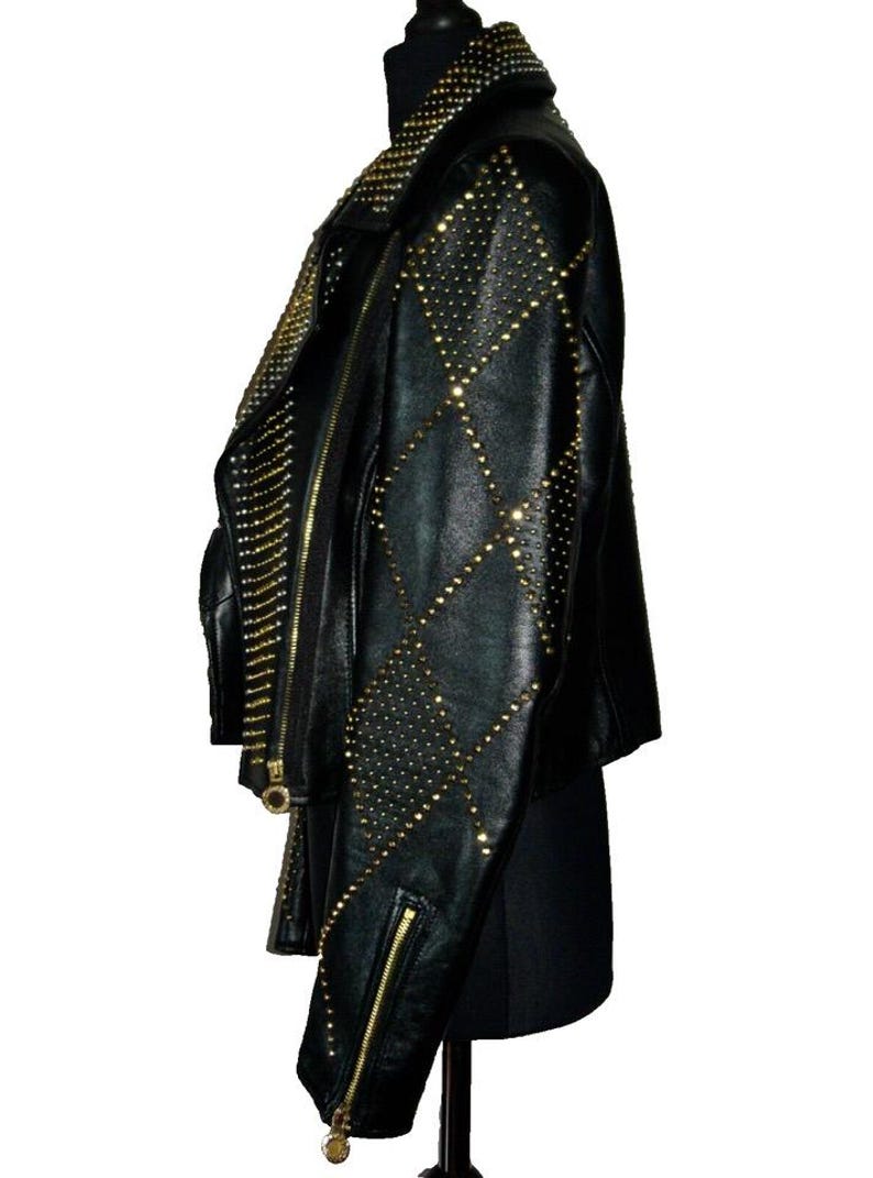 May include: A black leather jacket with a diamond pattern and gold studs. The jacket has a zip closure and a collar.