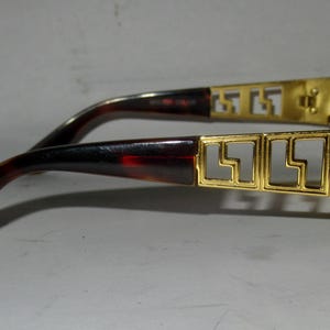 May include: Gold-tone sunglasses with a tortoiseshell frame and a Versace logo on the side. The sunglasses have a geometric design on the frame.
