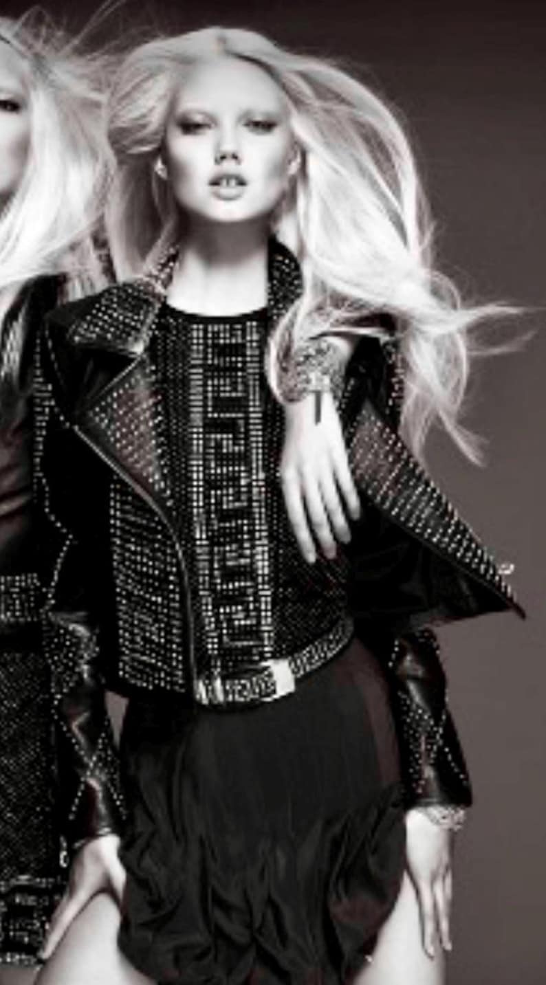 May include: A woman wearing a black leather jacket with silver studs and a black skirt with a silver pattern. She has long, straight, white hair and is wearing a silver bracelet on her wrist.