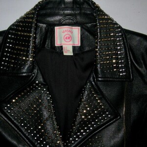 May include: Black leather jacket with a studded collar and a pink label that says "Versace Jeans Couture" and "VM".