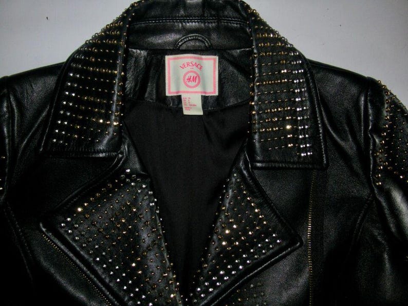 May include: Black leather jacket with a studded collar and a pink label that says "Versace Jeans Couture" and "VM".