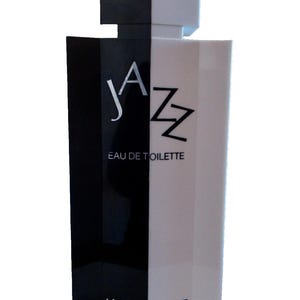 Op de afbeelding: Een rechthoekige parfumfles, verticaal verdeeld in zwart en wit. Het woord "JAZZ" staat in het wit op de zwarte kant, met "EAU DE TOILETTE" eronder. Het Yves Saint Laurent-logo staat onderaan.