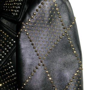 May include: Black leather jacket with gold studs in a geometric pattern. The jacket has a collar and a zip closure.