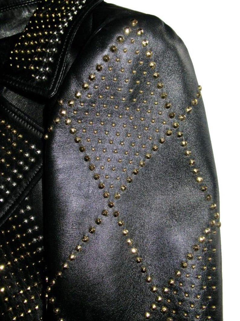 May include: Black leather jacket with gold studs in a geometric pattern. The jacket has a collar and a zip closure.