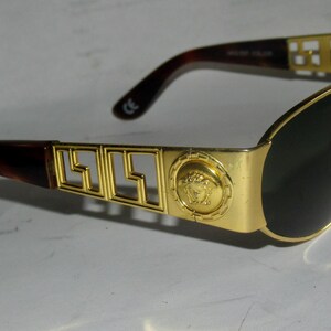 May include: Gold-tone sunglasses with black lenses and a brown tortoise shell frame. The frame features a gold metal design with the Versace logo and a Medusa head.