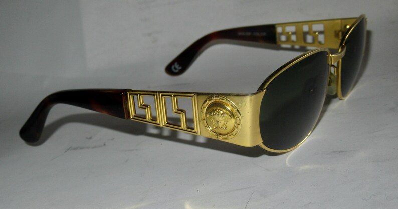 May include: Gold-tone sunglasses with black lenses and a brown tortoise shell frame. The frame features a gold metal design with the Versace logo and a Medusa head.
