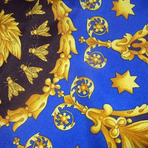 Puede incluir: Una tela azul con un patr&oacute;n dorado de flores estilizadas, estrellas y una cara. La tela tiene un fondo azul oscuro con un patr&oacute;n dorado.