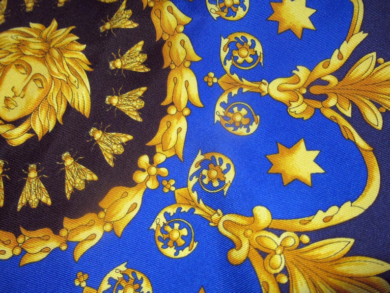 Puede incluir: Una tela azul con un patr&oacute;n dorado de flores estilizadas, estrellas y una cara. La tela tiene un fondo azul oscuro con un patr&oacute;n dorado.