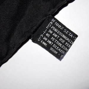 Puede incluir: Etiqueta de tela negra con texto blanco que dice "100% SETA - S", "PROFESSIONALLY", "30 NOT USE PER", "T08 PETROLEUM", "DO NOT BLEACH", "COOL", "IRON!"