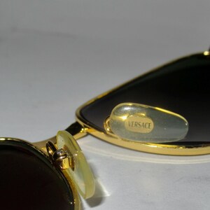 May include: Gold-tone sunglasses with dark lenses and a Versace logo on the nose pads.