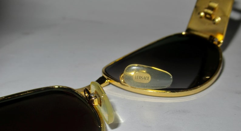 May include: Gold-tone sunglasses with dark lenses and a Versace logo on the nose pads.