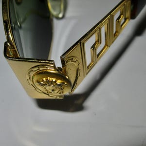 May include: Gold-toned sunglasses with a Versace logo on the arm and a Medusa head design on the frame.