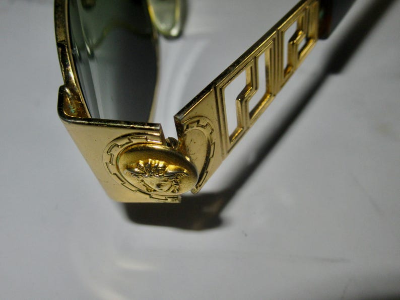 May include: Gold-toned sunglasses with a Versace logo on the arm and a Medusa head design on the frame.