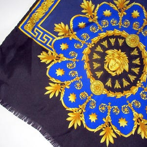 Puede incluir: Un pa&ntilde;uelo de seda negro y azul con un patr&oacute;n dorado y azul. El patr&oacute;n presenta un medall&oacute;n central con una cara estilizada y abejas, rodeado de un dise&ntilde;o repetitivo de estrellas, hojas y volutas.