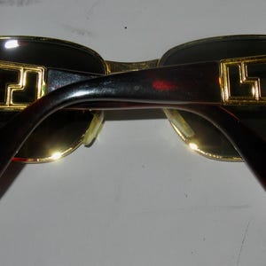 May include: Gold-tone sunglasses with black frames and dark lenses. The arms of the sunglasses have a gold-tone pattern.