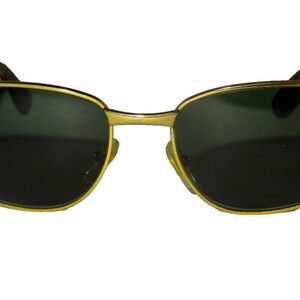 May include: Gold-tone sunglasses with dark lenses. The sunglasses have a rectangular shape and a thin metal frame.