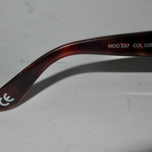 May include: Close-up of the brown tortoiseshell temple arm of a pair of eyeglasses. The arm is marked with the text "MOD.S37 COL.030" and the CE mark.